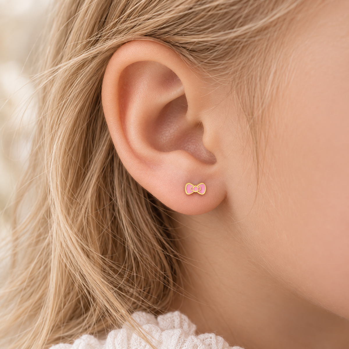 Pink bow hypoallergenic earring worn in a child’s ear, designed for sensitive ears